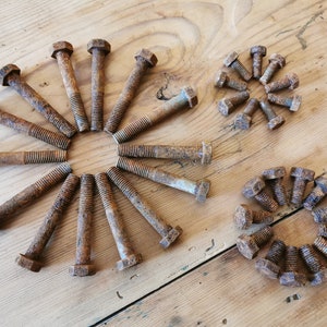 Puede incluir: Una colección de tornillos de metal oxidados dispuestos en tres patrones circulares. Los tornillos son de varios tamaños y tienen una textura rugosa y envejecida.