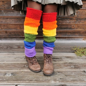 Op de afbeelding: Regenboog gestreepte beenwarmers gemaakt van gebreid garen. De beenwarmers worden gedragen over bruine laarzen.