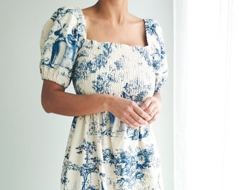 May include: A white midi dress with a blue and white toile pattern. The dress has a square neckline, puffed sleeves, and a fitted bodice.
