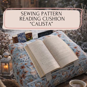 Peut inclure: Un coussin de lecture bleu clair avec un motif floral et sur le thème du café, tenant un livre ouvert. Le texte sur l'image indique "SEWING PATTERN READING CUSHION 'CALISTA'". Une tasse de café est à proximité.