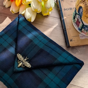 Peut inclure: Un carré de poche plié à carreaux bleu marine et vert d'eau, orné d'une épingle abeille dorée. Le carré de poche est posé sur une surface en bois, avec un livre et des fleurs en arrière-plan. L'épingle abeille est un accessoire décoratif.