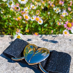 Peut inclure: Une ceinture élastique noire avec une boucle en forme de cœur dorée. La boucle est brillante et reflète l'environnement environnant.