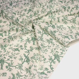 K&ouml;nnte beinhalten: Ein St&uuml;ck cremefarbener Stoff mit einem sich wiederholenden gr&uuml;nen Toile-Muster. Das Design besteht aus detaillierten Illustrationen von V&ouml;geln, die auf bl&uuml;henden Zweigen und bebl&auml;tterten Ranken sitzen und eine dichte, durchgehende botanische Szene bilden.