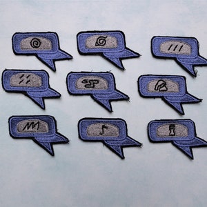 May include: Ten blue and grey embroidered patches with different symbols, including a swirl, a spiral, three lines, a kanji character, a cloud, a circle with a line through it, a mountain, a tree, and a bottle. The patches are shaped like speech bubbles.