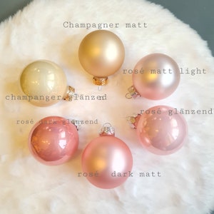 Pu&ograve; includere: Sei palline di Natale in varie tonalit&agrave; di champagne e rosa. Gli ornamenti sono etichettati con testo che indica la loro finitura: opaca o lucida. I colori vanno dall'oro chiaro al rosa scuro, su uno sfondo bianco morbido e soffice.