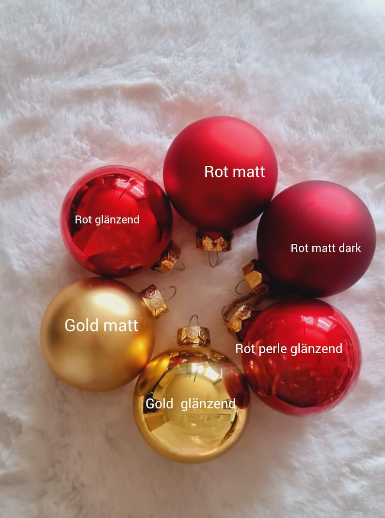 Pu&ograve; includere: Una collezione di decorazioni natalizie in varie tonalit&agrave; di rosso e oro. Le decorazioni includono finiture opache e lucide, con etichette di testo in tedesco. Le decorazioni sono disposte a cerchio.