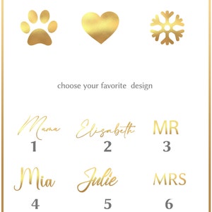 Pu&ograve; includere: Sfondo bianco con disegni dorati: impronta di zampa, cuore e fiocco di neve. Opzioni di testo dorate: "Mama", "Elisabeth", "MR", "Mia", "Julie" e "MRS", con i numeri da 1 a 6 sotto.
