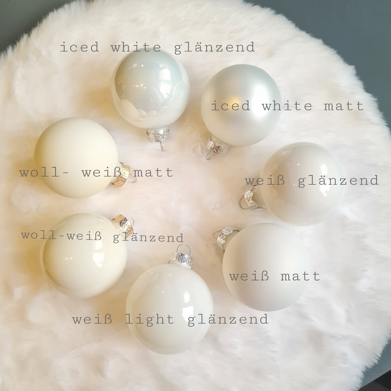 Pu&ograve; includere: Una collezione di ornamenti natalizi bianchi con varie finiture, tra cui opaca, lucida e iridescente. Gli ornamenti sono disposti su una superficie bianca e soffice, con etichette di testo che indicano i diversi stili.