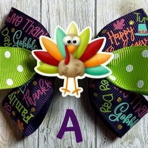 May include: A purple and green hair bow with a Thanksgiving turkey design. The bow has white polka dots and the text "Give Thanks" and "Happy Thanksgiving" on it.