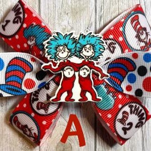 May include: A red, white, and blue bow with a white background. The bow features a red and white polka dot pattern, a blue and white striped pattern, and a white pattern with red polka dots and Thing 1 and Thing 2 from the book "The Cat in the Hat".