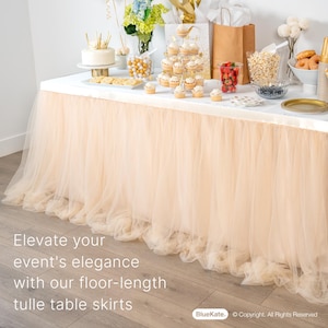 May include: A peach tulle table skirt drapes over a white table with a variety of party decorations, including cupcakes, a cake, and a bowl of popcorn. The text "Elevate your event's elegance with our floor-length tulle table skirts" is visible at the bottom of the image.
