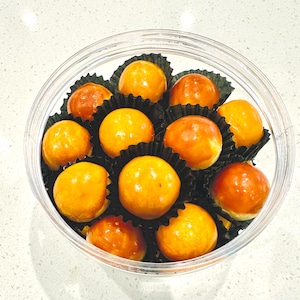 May include: A clear glass jar filled with small, round, orange-colored pastries. The pastries are arranged in a circular pattern and are surrounded by black paper cupcake liners.