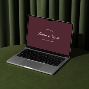 May include: A silver laptop displaying a burgundy screen with the text "The Wedding of Laura & Ryan" and "At Baloon Bay, Modena." The laptop is open on a green surface, with a dark green curtain in the background.