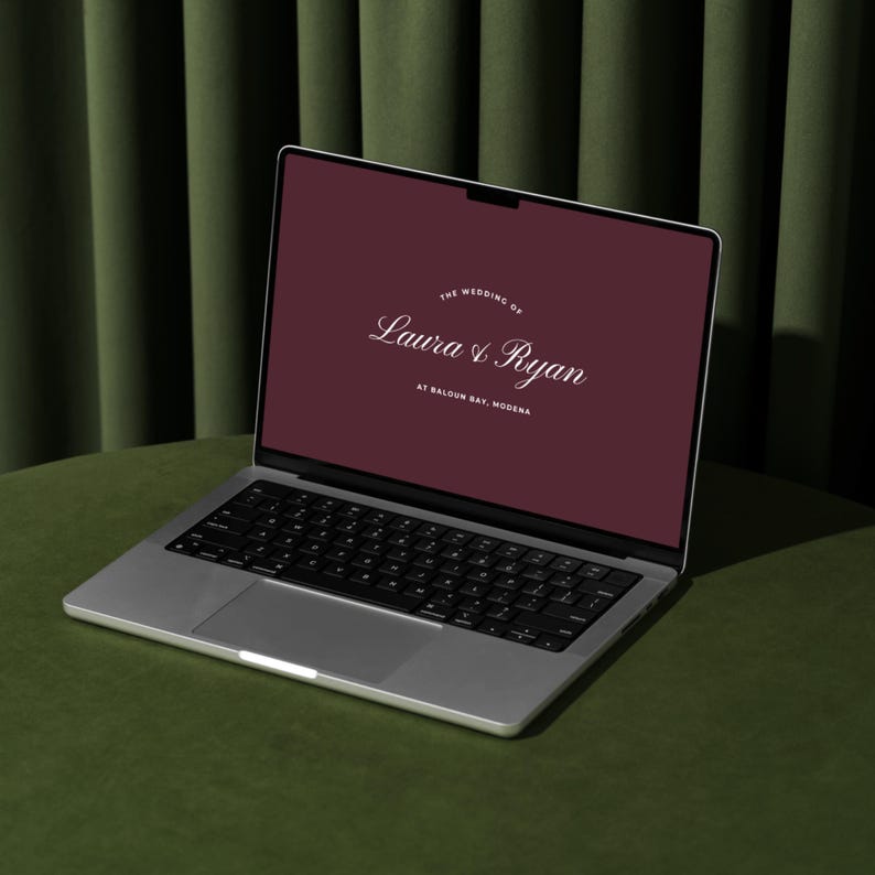 May include: A silver laptop displaying a burgundy screen with the text "The Wedding of Laura & Ryan" and "At Baloon Bay, Modena." The laptop is open on a green surface, with a dark green curtain in the background.