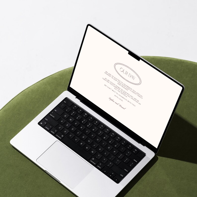 May include: A silver laptop with a black keyboard and a white trackpad sits on a green chair. The laptop screen displays the words "OUR DAY" in an oval design, along with additional text. The laptop is open and angled.