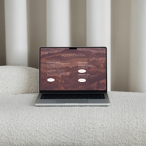 May include: A silver laptop displaying a website with the word "ACCOMMODATION" at the top. The website features text and images of hotels. The laptop is open on a white, textured surface.