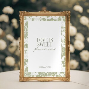 May include: A gold-framed sign with the text "LOVE IS SWEET please take a treat" in elegant script. The sign has a white background with a delicate green lace pattern border. The names "SOPHIA and JAMES" are at the bottom.