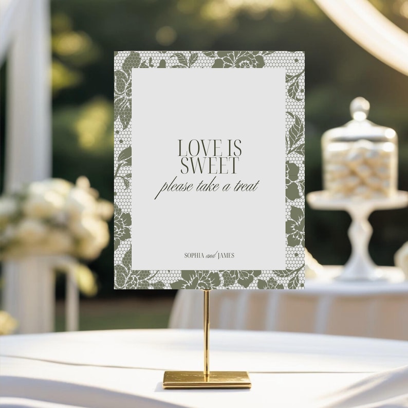 May include: A wedding sign with the text "LOVE IS SWEET please take a treat" in elegant script. The sign has a floral lace border and is displayed on a gold stand. The names "SOPHIA and JAMES" are at the bottom.