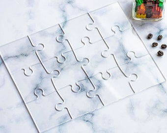 May include: A clear acrylic jigsaw puzzle with 12 pieces, each shaped like a jigsaw puzzle piece. The puzzle is on a white marble surface.