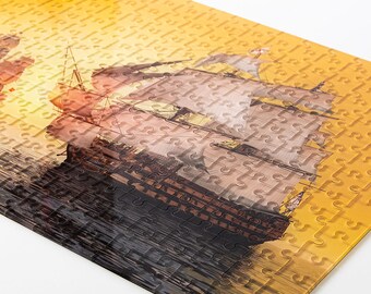 May include: A close-up of a jigsaw puzzle depicting a large sailing ship with white sails against a yellow sunset background. The puzzle pieces are visible and the image is slightly blurred.