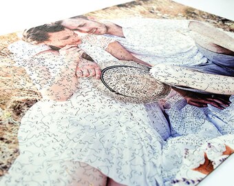 May include: A couple pose for a photograph in a field. The woman is wearing a white dress with a lace pattern. The man is wearing a white shirt and trousers. They are both smiling and looking at the camera.