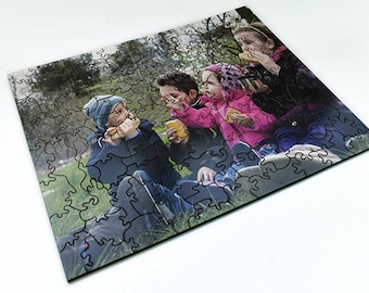 May include: A jigsaw puzzle featuring a photo of four children sitting on a grassy area, eating snacks. The children are wearing casual clothing and are smiling. The puzzle pieces are black and white.