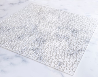 May include: A white jigsaw puzzle with all the pieces in place. The puzzle is on a white marble surface.