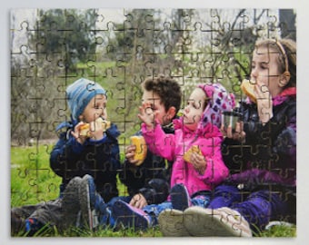 May include: Four children sitting on the grass eating snacks. The children are wearing colourful clothing and hats. They are all smiling and looking at the camera.