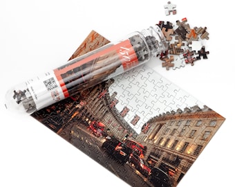 May include: A 150-piece jigsaw puzzle of a street scene in London, England. The puzzle is complete and laid out on a white surface. The puzzle pieces are white with a printed image of a street scene with buildings, cars, and people. The puzzle is in a clear plastic tube with a red and white label that says "150".
