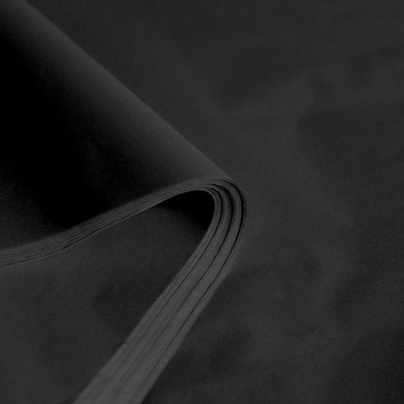 May include: Black tissue paper, folded in a stack, showing the texture and colour of the paper.