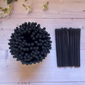 May include: A close-up of a bundle of black matches. The matches are arranged in a circle and are all the same size. The matches are on a white surface.