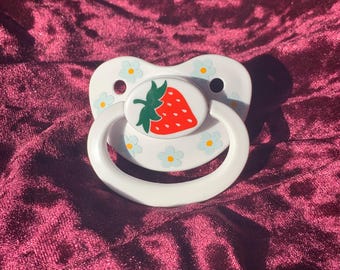 May include: White pacifier with a red strawberry design and blue flower accents.