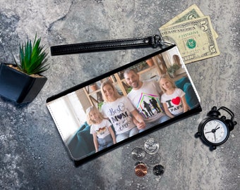 Puede incluir: Cartera negra con foto familiar, correa de muñeca negra y un pequeño despertador negro. La cartera muestra una familia de cuatro con camisetas a juego. También hay dos billetes de cinco dólares y algunas monedas.