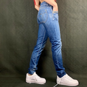 May include: A person wearing blue denim jeans with a light wash and white trainers.