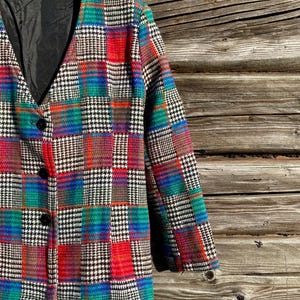 Pode incluir: Um blazer vintage com um design de patchwork em uma variedade de cores, incluindo vermelho, azul, verde e preto. O blazer tem uma gola clássica, três botões pretos e um forro preto. O casaco está pendurado em um cabide de madeira.