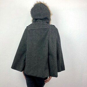 May include: A charcoal gray cape with a hood trimmed with faux fur. The hooded cape has a button closure and a classic design. The cape is made of a soft, warm material, perfect for cold weather.