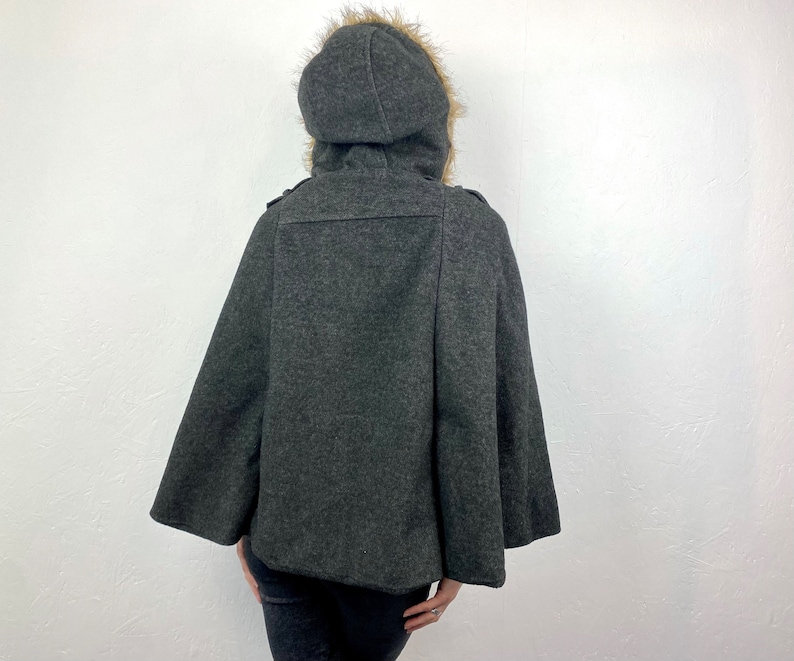 May include: A charcoal gray cape with a hood trimmed with faux fur. The hooded cape has a button closure and a classic design. The cape is made of a soft, warm material, perfect for cold weather.