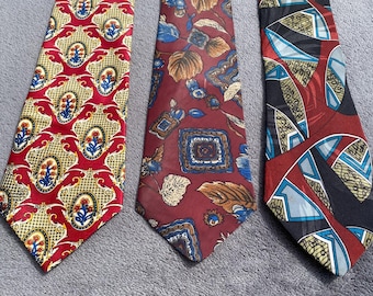 Può includere: Tre cravatte fantasia. Una è rossa con un motivo floreale oro e blu. Un'altra è bordeaux con forme floreali e geometriche blu e marroni. La terza è rossa, nera e blu con forme astratte.