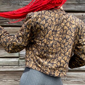 May include: A brown and gold leaf patterned cropped jacket with long sleeves.