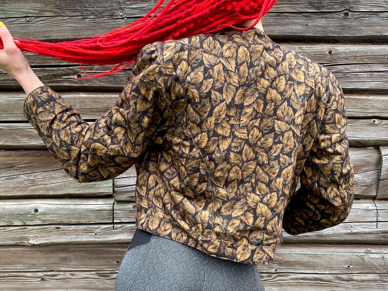 May include: A brown and gold leaf patterned cropped jacket with long sleeves.