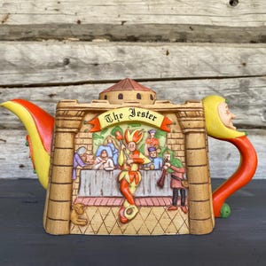 以下が含まれることがあります： 道化師のシーンを特徴とする、気まぐれなデザインのセラミックティーポット。 ティーポットは、赤と黄色の注ぎ口とハンドルが付いたタンベースです。 ティーポットの前面には、道化師やその他の人物のレリーフがあります。 テキスト「The Jester」はバナーにあります。