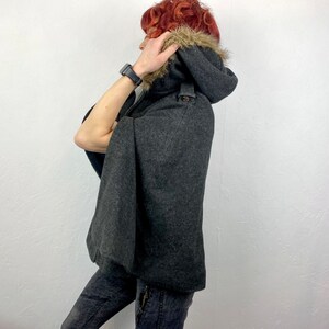 May include: A dark gray hooded cape with a faux fur trim around the hood. The cape has a button closure and a classic design. The garment is made of a wool-like material, offering warmth and style. A fashionable outerwear piece.