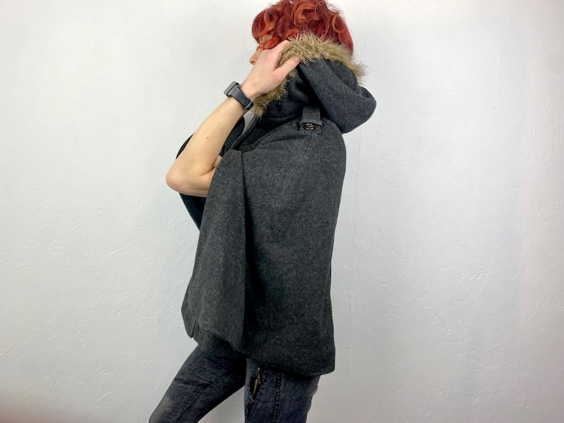 May include: A dark gray hooded cape with a faux fur trim around the hood. The cape has a button closure and a classic design. The garment is made of a wool-like material, offering warmth and style. A fashionable outerwear piece.