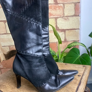 Könnte beinhalten: Schwarze, kniehohe Lederstiefel mit spitzer Zehenpartie und hohem Absatz. Die Stiefel haben ein genähtes Design und sind aus Leder und Wildleder.