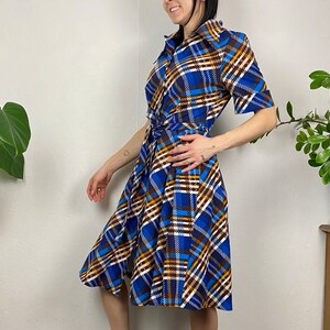May include: A blue, brown, and white plaid wrap dress with a short sleeve and a tie belt.