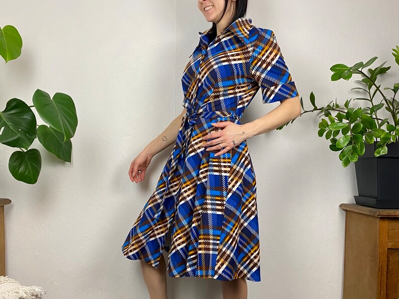May include: A blue, brown, and white plaid wrap dress with a short sleeve and a tie belt.