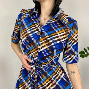 May include: A blue, brown, and white plaid dress with a button-up front and a tie belt. The dress has short sleeves and a collared neckline.