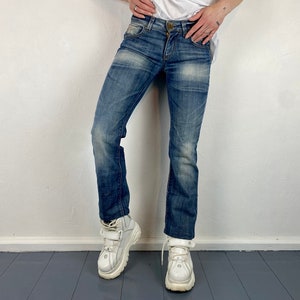 Può includere: Un paio di jeans blu denim a gamba dritta. I jeans hanno un lavaggio chiaro e sono indossati con sneakers bianche con plateau.