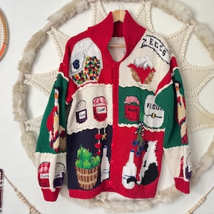 Può includere: Un cardigan vintage con bottoni e design patchwork. Il maglione presenta pannelli rossi, verdi e bianchi con varie immagini e testi relativi al cibo, tra cui "EGGS" e "FLOUR". Il colletto e i polsini sono rossi.