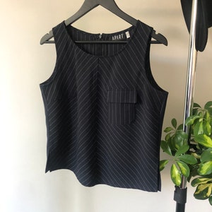Puede incluir: Una blusa sin mangas de rayas blancas y negras con un bolsillo en la parte delantera. La blusa tiene la palabra "APART" impresa en la etiqueta.